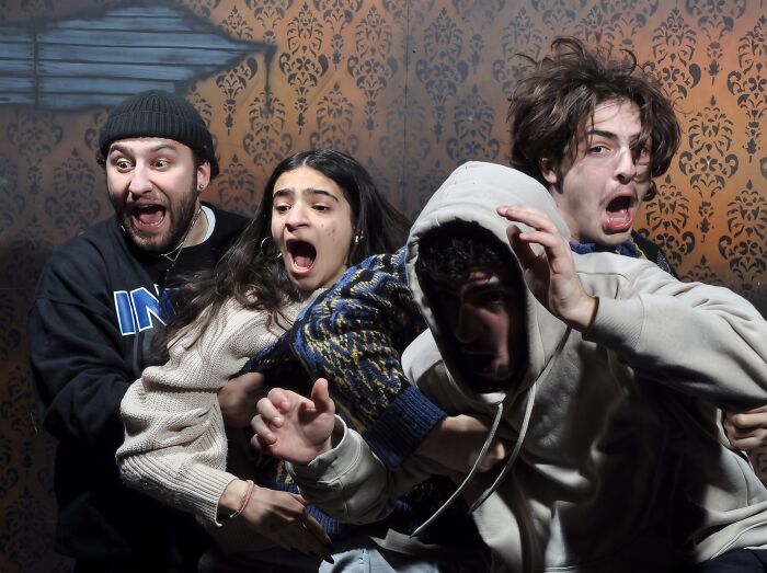 Four young people screaming in fear inside a haunted house reaction photo.
