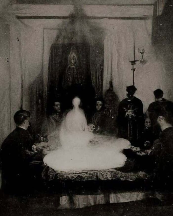 An eerie dark seance gathering with a glowing figure, captured in a eerie horror movie style photo.