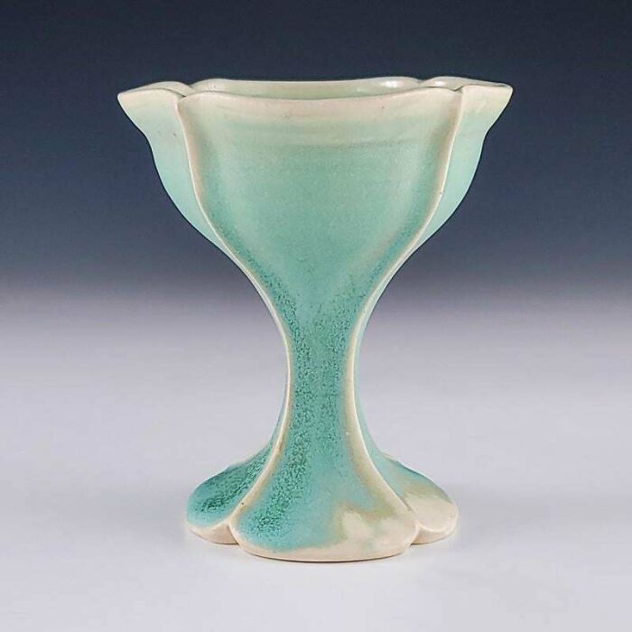 An elegant light teal chalice-shaped vase displaying handmade pottery creations.