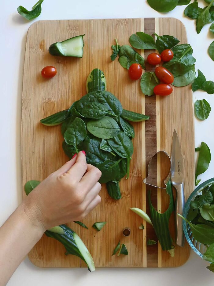 Sarah Rosado food art of a turtle being made on a cutting board using green spinach leaves and cucumbers.