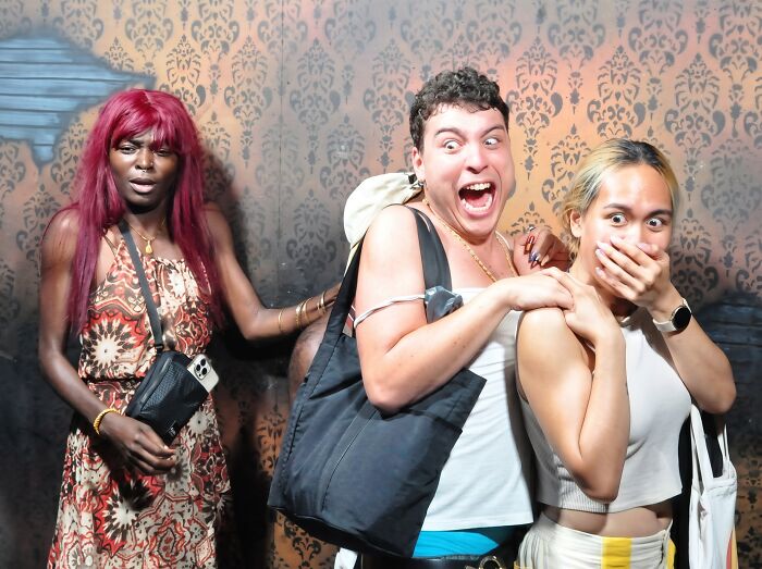 Hilarious haunted house photo capturing three friends reacting with extreme terror inside a dark maze.