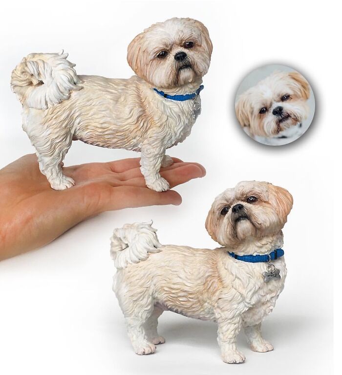 Small, hyperrealistic pet sculptures of a fluffy white Shih Tzu wearing a blue collar with a name tag