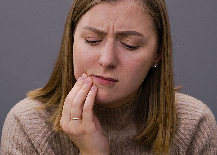 A woman holding her jaw in discomfort, reflecting physical challenges during new motherhood.
