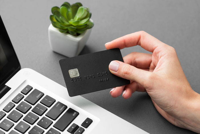 A hand holding a black credit card near a laptop, symbolizing financial disputes in divorce stories.